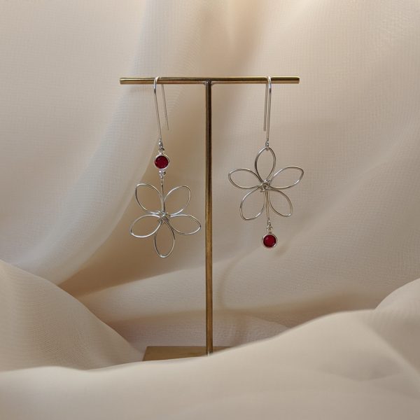 Silver flora earrings with red gem hanging on stand